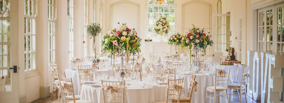 The Orangery function room, well lit from the large windows and setup for a banquet with floral table centers. 